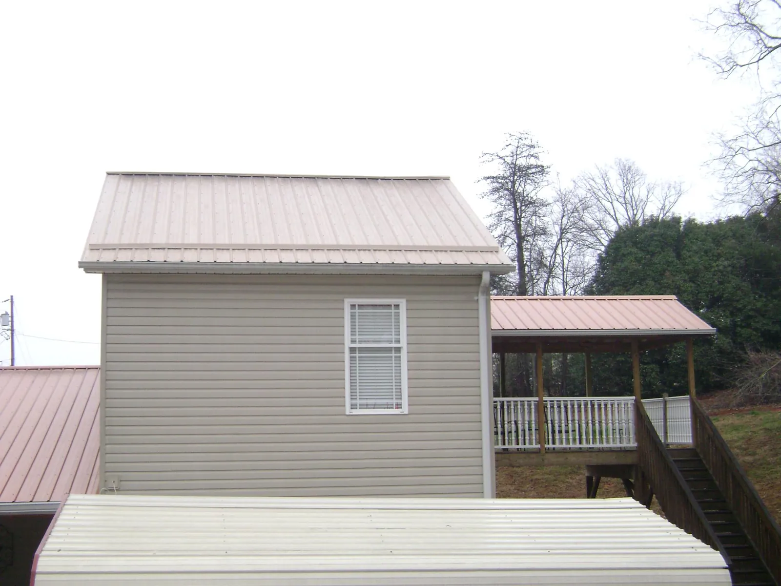 Tan metal roofs on a two story addition and attached porch, from a Roof Replacement job in Independence